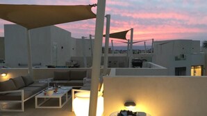 A rooftop terrace with outdoor seating, including a sofa and a table, under a large umbrella.