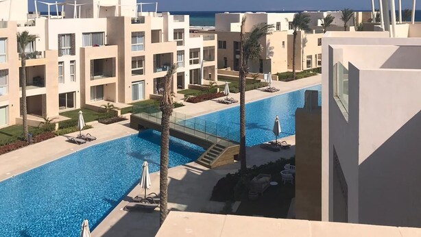 A resort with a swimming pool, palm trees, and a view of the ocean.