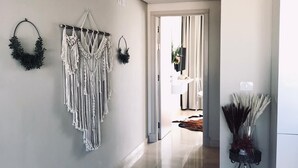 A hallway with a macrame wall hanging, a wreath, and a plant on a stand.