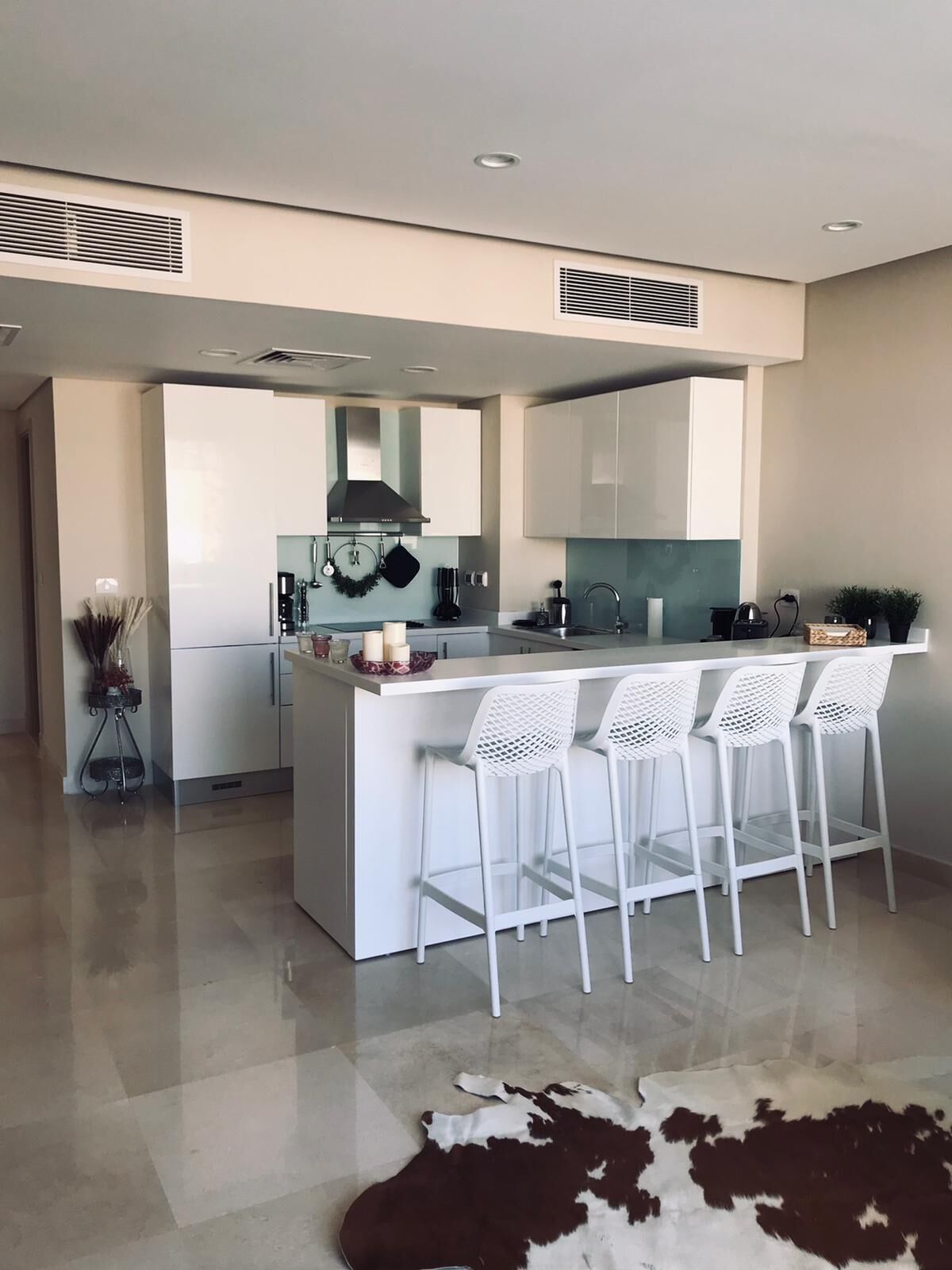 Een moderne keuken met een centraal eiland, witte barstoelen en een koeienhuidtapijt op de vloer.