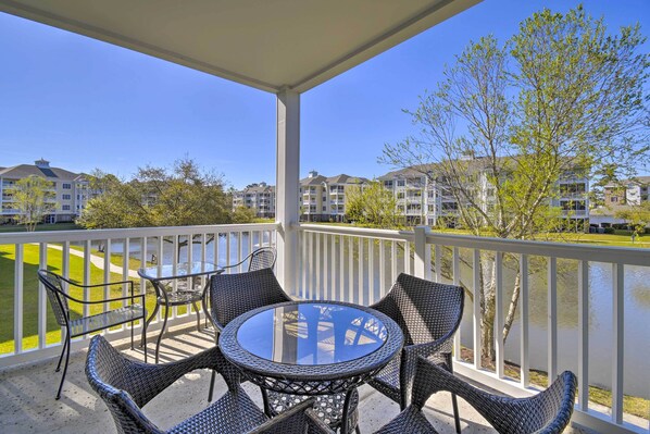 A balcony with a round table and chairs, overlooking a body of water and a row of buildings. - Access to 7 Pools: Myrtlewood Golf Condo! (Myrtle Beach)