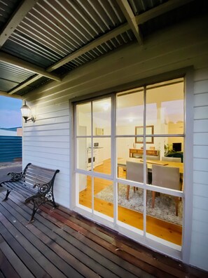 A covered patio with a wooden bench, a large sliding glass door leading to an interior dining area with a table and chairs. - Bushby’s Self Contained Cottage (Dunolly)
