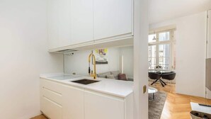 Una cocina moderna con armarios blancos, un grifo dorado y vistas a un comedor con una mesa redonda y sillas.
