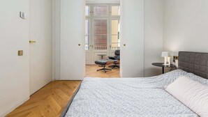 Un dormitorio con una cama, una mesita de noche, una silla y vistas a un balcón a través de una puerta abierta.