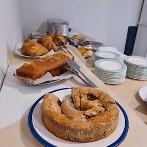 A buffet table with various baked goods including a large cake on a blue plate, croissants, and other pastries. - Hotel pixunte (Santa Marina)
