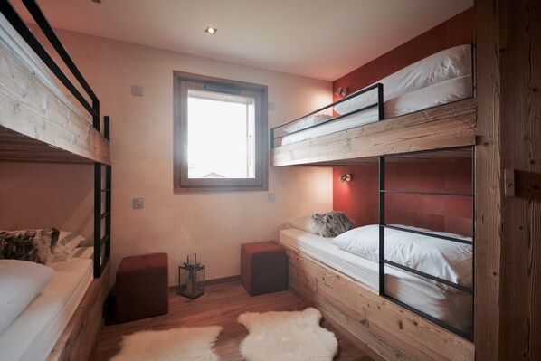 A bunk bed room with a window, a small table, and a fur rug.