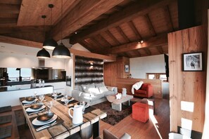 A modern interior with a wooden ceiling, a dining area with a long table set for four, a grey sofa, and a red chair. - Chalet Hanadama Collection Perles (Bolquère)