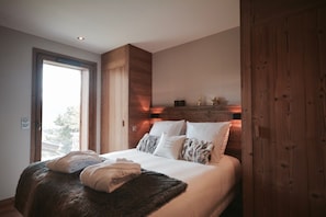 A bedroom with a large bed, wooden headboard, and a view through a window. - Chalet Hanadama Collection Perles (Bolquère)