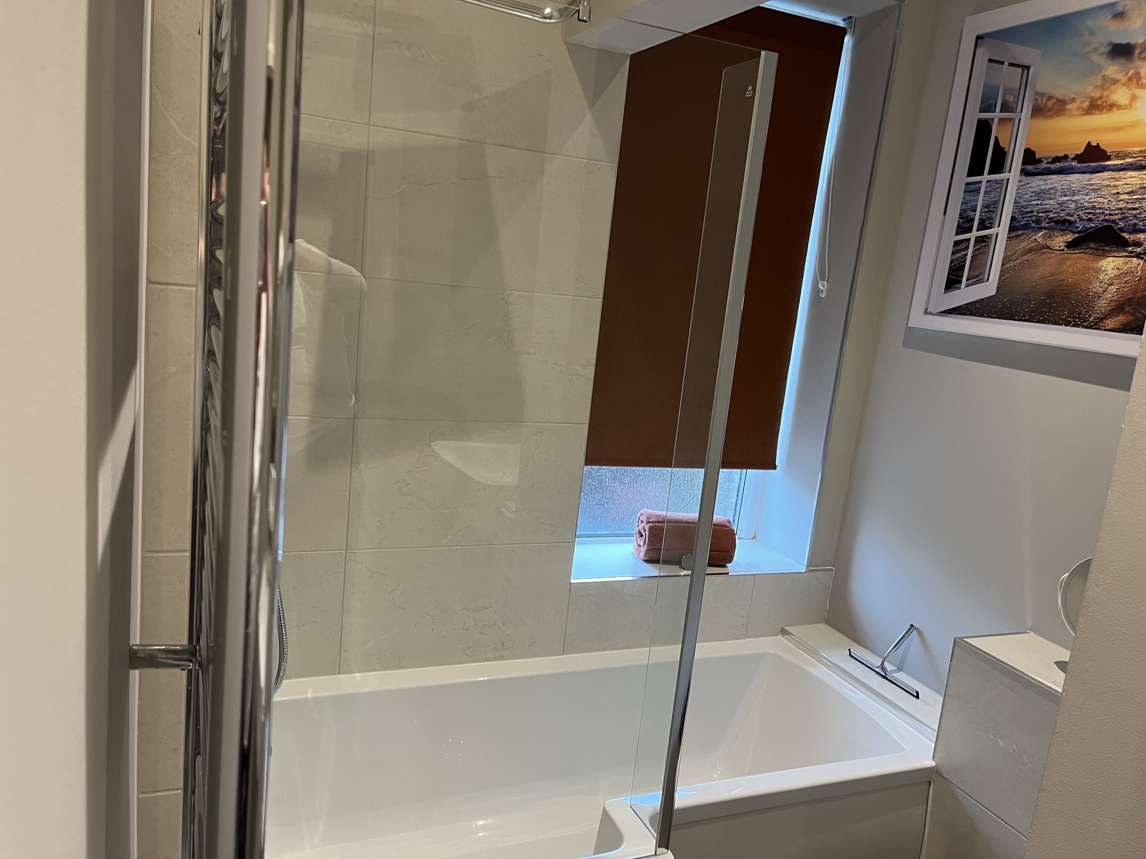 Ein modernes Badezimmer mit einer Glasdusche, einer weißen Badewanne und einem Fenster mit Meerblick.