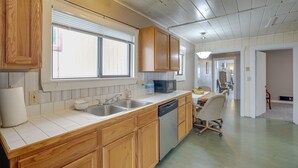 A kitchen with wooden cabinets, a dishwasher, a microwave, and a dining area with a table and chairs. - Hilltop Hideout w/ Sweeping Birch Bay Views (Blaine)