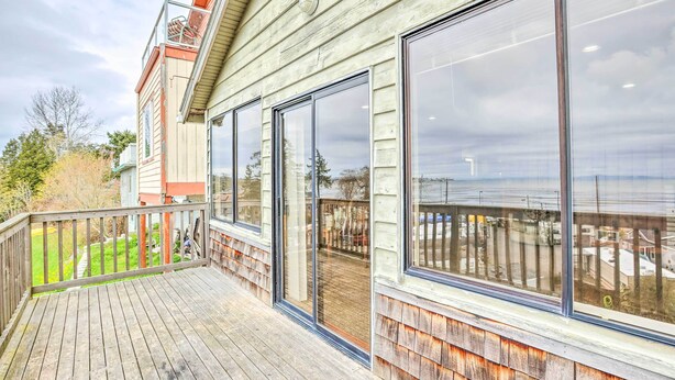 A wooden deck with large sliding glass doors leading to a covered outdoor area. - Hilltop Hideout w/ Sweeping Birch Bay Views (Blaine)