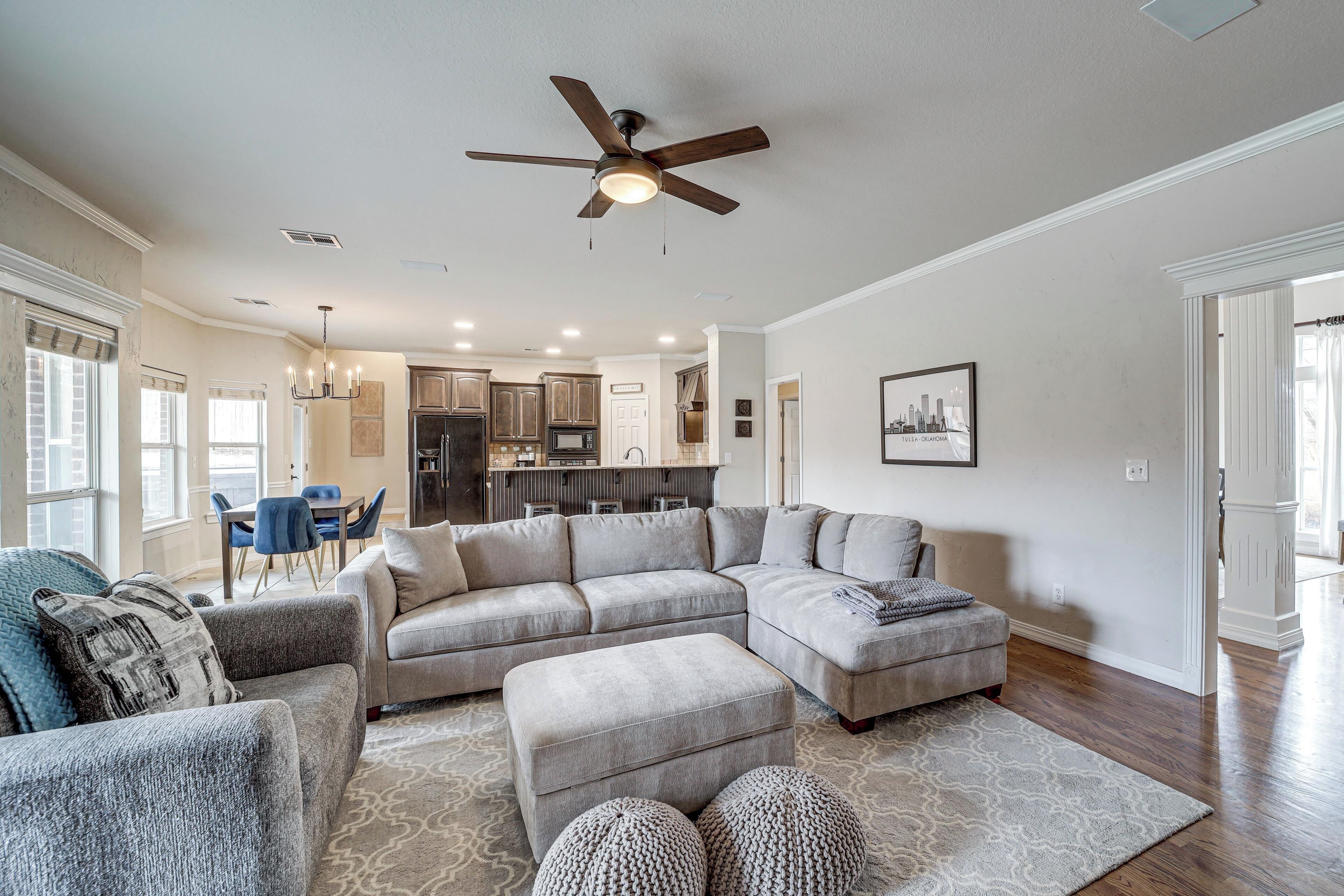 A spacious living room with a large sectional sofa, a ceiling fan, and a dining area with blue chairs.