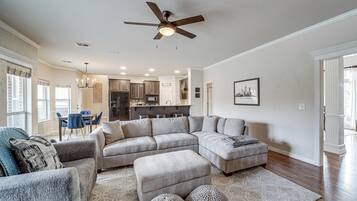 A spacious living room with a large sectional sofa, a ceiling fan, and a dining area with blue chairs.