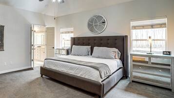 A bedroom with a large bed, a ceiling fan, a dresser, and a window with blinds.