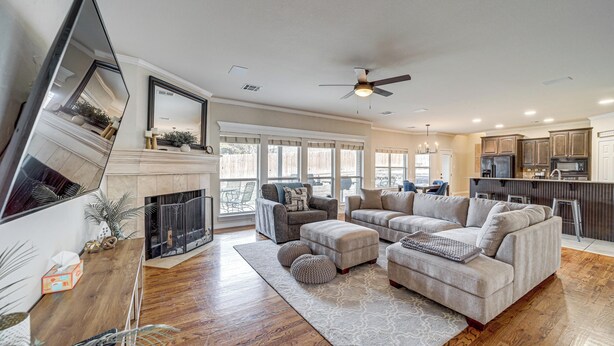 A spacious living room with a fireplace, large sofa, and ottomans. A kitchen with modern appliances is visible in the background. - Pet-Friendly Tulsa Escape w/ Private Hot Tub! (Tulsa)