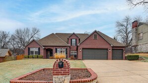 A two-story brick house with a stone fireplace, a garage, and a well-maintained lawn. - Pet-Friendly Tulsa Escape w/ Private Hot Tub! (Tulsa)