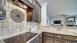 A kitchen with a central island, dark wooden cabinets, a tiled backsplash, and a built-in stove. - Pet-Friendly Tulsa Escape w/ Private Hot Tub! (Tulsa)