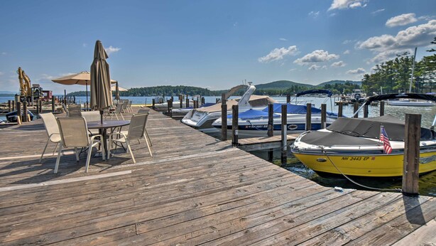 A wooden dock with tables and chairs, a yellow boat with an American flag, and a clear blue sky. - Gilford Escape w/ Boat Slip on Sanders Bay! (Gilford)