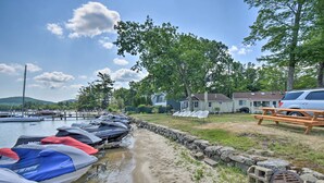 A marina with jet skis docked, a picnic table, and houses in the background. - Gilford Escape w/ Boat Slip on Sanders Bay! (Gilford)
