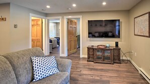 A living room with a grey sofa, wooden cabinet, and a television on the wall. - Gilford Escape w/ Boat Slip on Sanders Bay! (Gilford)