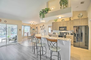 A modern kitchen with a central island, bar stools, stainless steel appliances, and decorative plants.