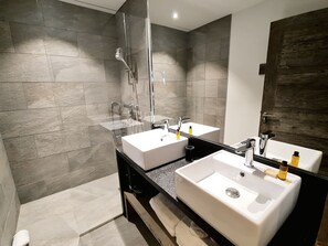 Ein modernes Badezimmer mit zwei Waschbecken, einer Dusche und einem großen Spiegel.