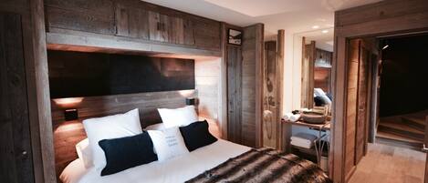 Une chambre avec un grand lit, une tête de lit en bois et un plaid en fourrure. On y trouve un bureau avec une chaise et un miroir.