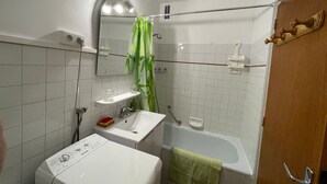 Un baño con lavamanos blanco, un espejo, una ducha con cortina verde y una puerta de madera.