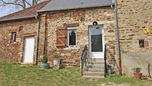 A stone house with a small front porch, a wooden door, and a window with shutters. - Charming renovated house with private terrace and garden (Rives-d'Andaine)