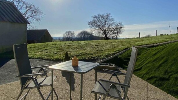 A patio with a table and chairs, a small decorative item on the table, and a grassy area with trees and a fence in the background. - Charming renovated house with private terrace and garden (Rives-d'Andaine)