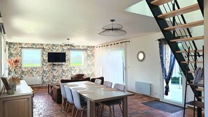 A dining area with a table and chairs, a television on the wall, and a staircase. - Charming cottage for 6 near Angers, countryside tranquility (Corzé)