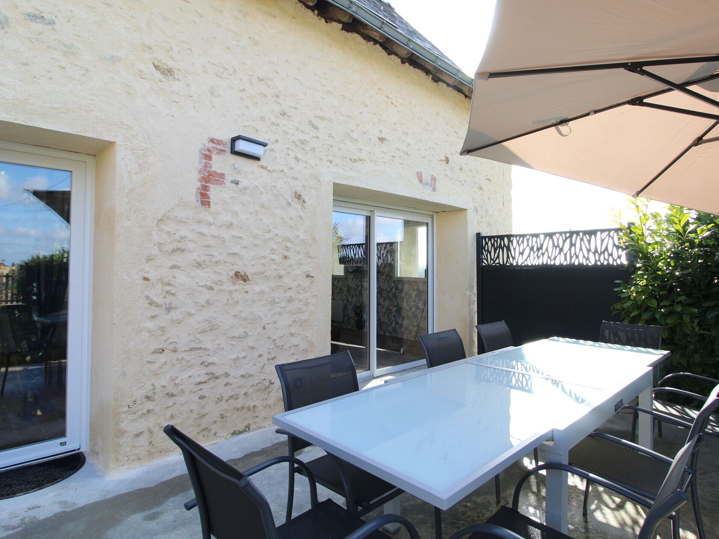 Een terras met een witte tafel en stoelen, een schuifpui en een overdekt gedeelte met een beige parasol.
