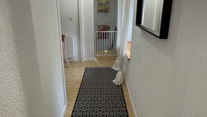 Een smalle gang met een kamerbreed tapijt, een witte deur en een spiegel aan de muur.