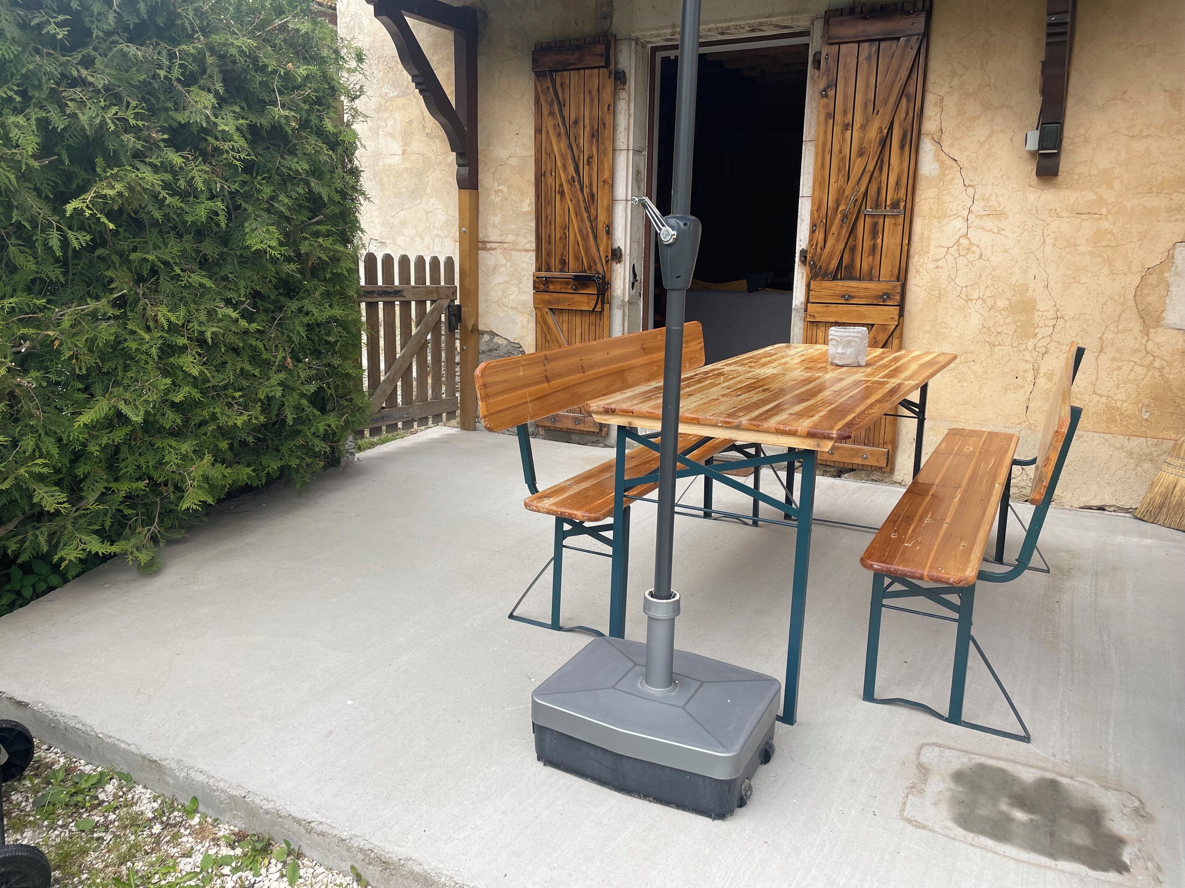 Una veranda esterna con tavolo e panche in legno, pavimento in cemento e recinzione in legno.