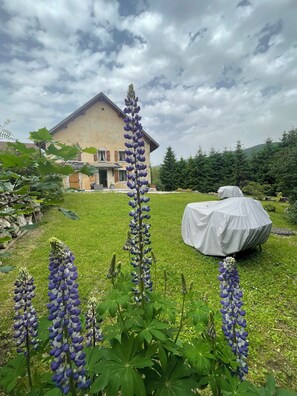 A house with a garden featuring tall purple flowers and a covered outdoor table. - Accommodations in a typical Vercors farmhouse, near the village. (Autrans-Méaudre en Vercors)