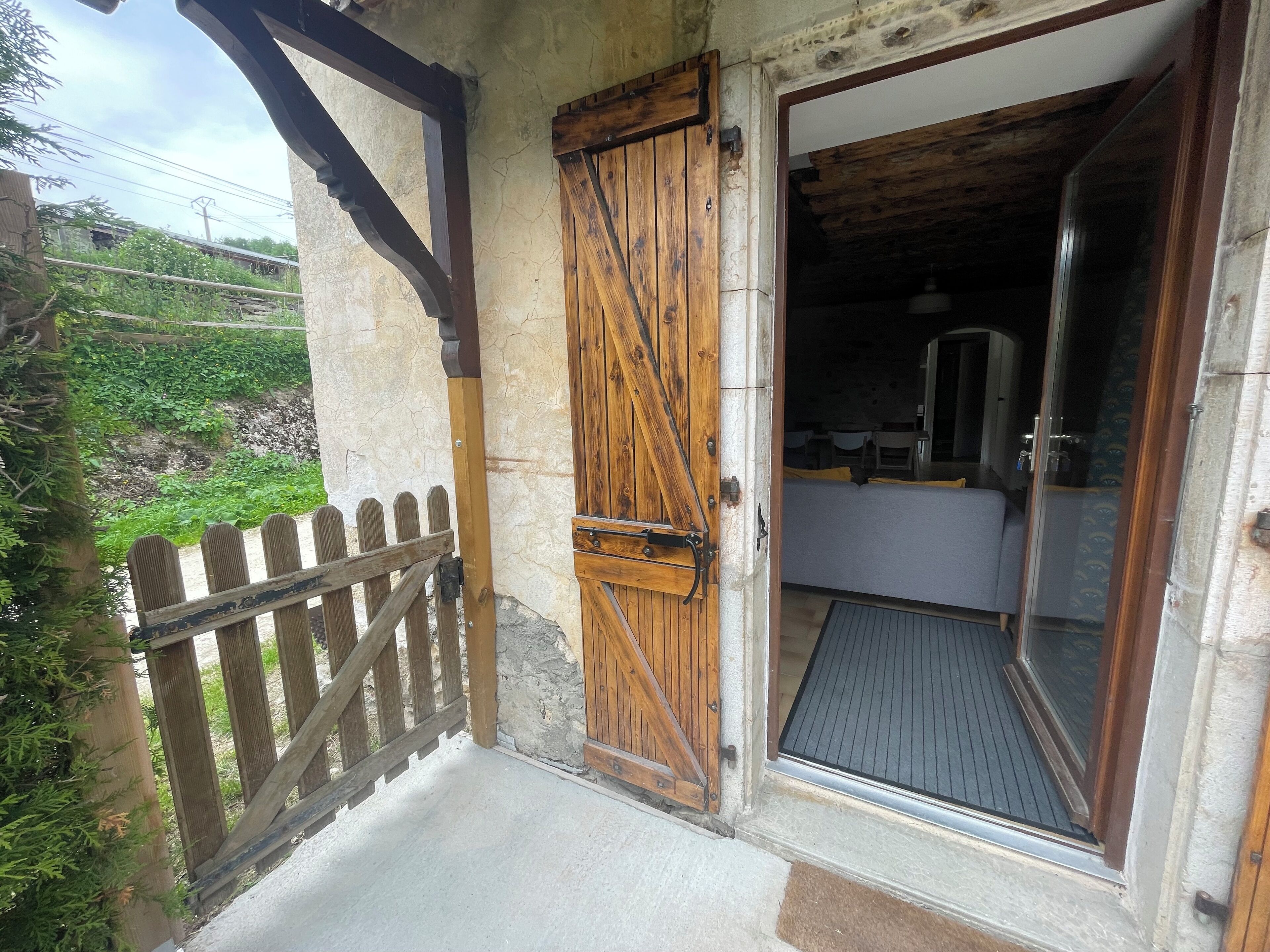 Une porte en bois rustique donne sur un espace cuisine aménagé avec un banc et une petite table.