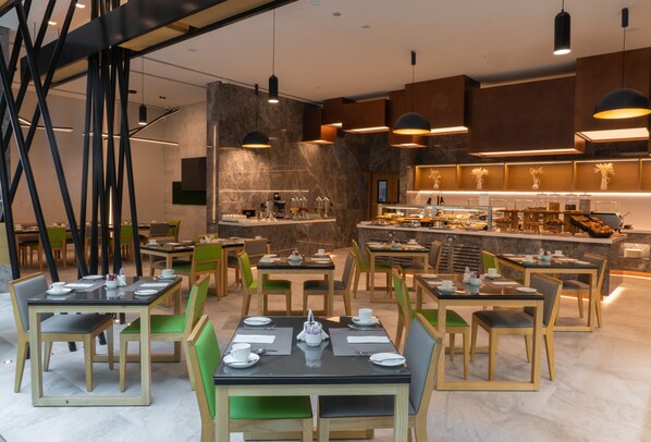 Un restaurante moderno con varias mesas y sillas, una zona de cocina e iluminación colgante.