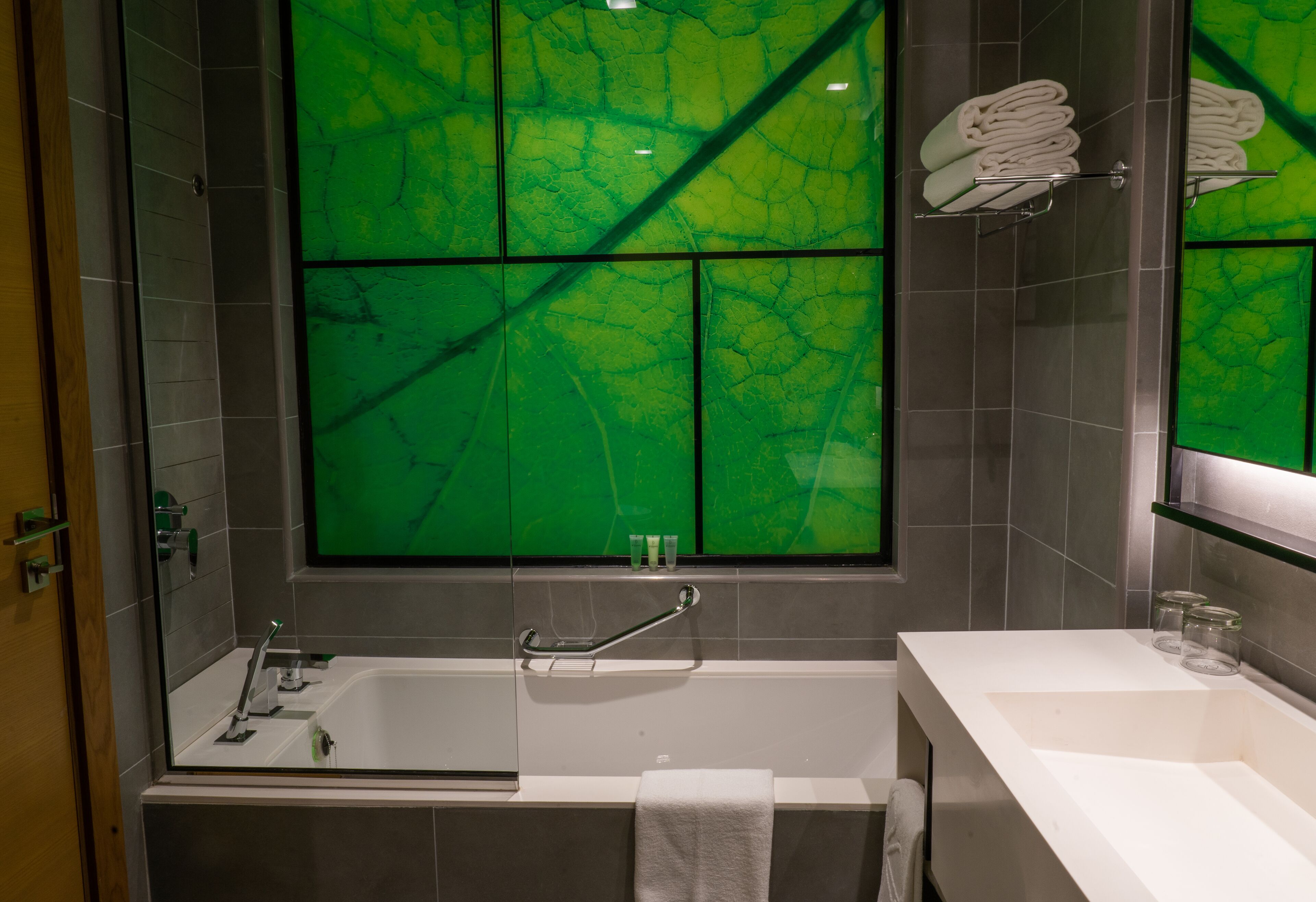 A modern bathroom with a bathtub, a vanity with a mirror, and a green-tinted window.