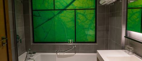 A modern bathroom with a bathtub, a vanity with a mirror, and a green-tinted window.