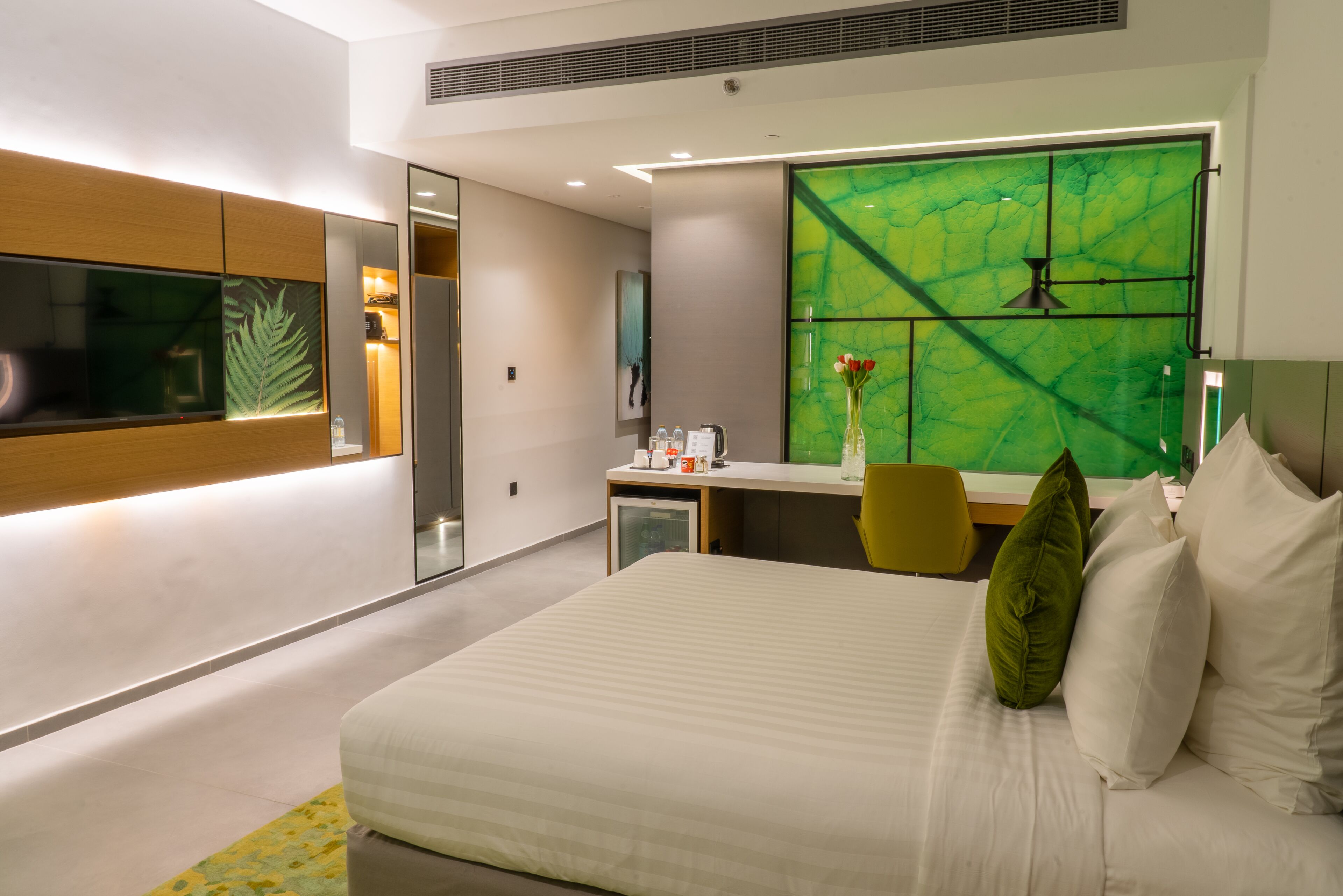 A modern hotel room with a large bed, a desk, and a green-tiled wall.