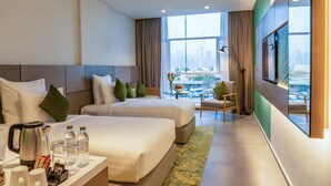 A hotel room with two beds, a coffee maker, water bottles, a desk with a lamp, and a view of the cityscape. - Al Khoory Courtyard Hotel (Dubai)