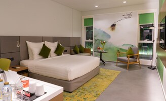 Una habitación de hotel moderna con una cama grande, una mesita con artículos de aseo, una silla y un ventanal con marco verde.