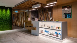 A modern reception area with a wooden reception desk, a green wall, and a marble wall with a wooden slat design. - Al Khoory Courtyard Hotel (Dubai)