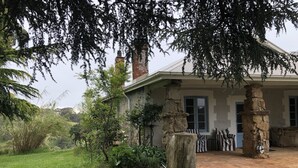 Een stenen huis met een veranda, omringd door groen en een grindpad.