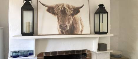A fireplace with a brick surround, a framed picture of a cow's face, and two black lanterns on either side.