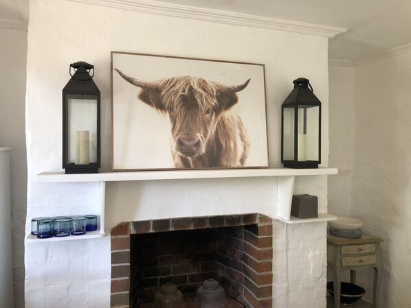 A fireplace with a brick surround, a framed picture of a cow's face, and two black lanterns on either side.