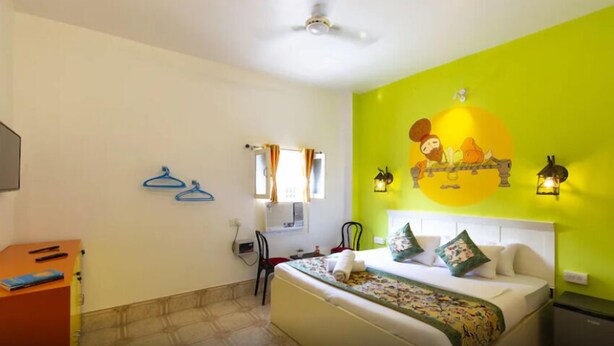 A hotel room with a bed, a desk, a chair, a wardrobe, and a wall with a mural. - WANDER STATION VARANASI (Varanasi)