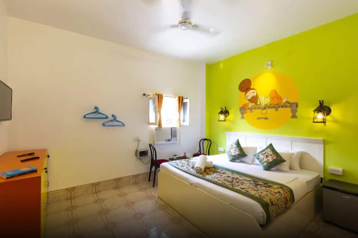 Habitació d'hotel amb llit, escriptori, cadira, armari i una paret amb mural.