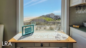 Une cuisine avec vue sur la plage, une table en bois recouverte d’une nappe en dentelle et un panneau sur lequel on peut lire : « Passez plus de temps à la plage, et moins de temps à vous inquiéter ».