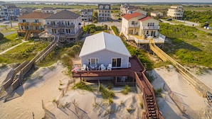 Une propriété située en bord de mer, comprenant plusieurs maisons, dont une grande maison blanche dotée d’une terrasse couverte et d’un espace salon extérieur.